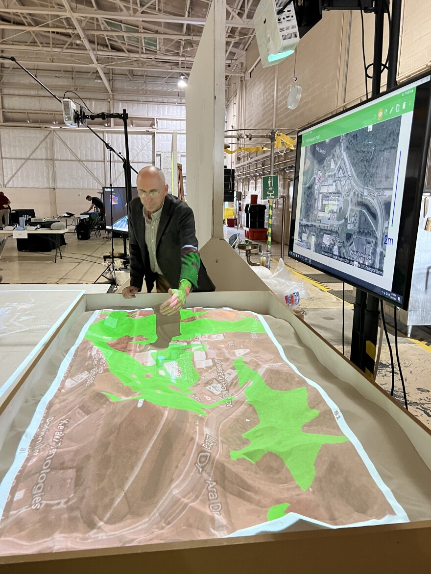 Charles Amburn, science and technology manager at the DEVCOM soldier center, demonstrates using a physical sand table with a map that can be used by the military during the Yuma Proving Ground Project Convergence Technology Gateway on Monday, Oct. 17, 2022.