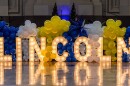  A arge lighted sign that reads "Lincoln" sits on a shiny floor surrounded by white, yellow and blue balloons.