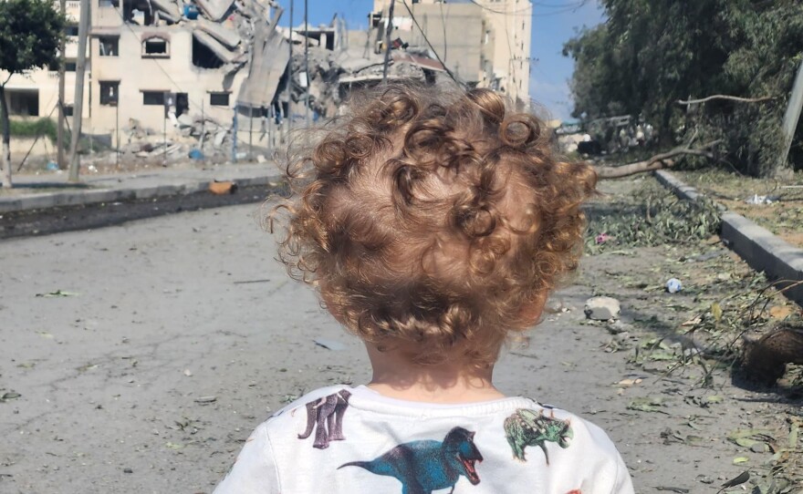 A 2-year-old baby boy stands in a street in Gaza where buildings have been destroyed.