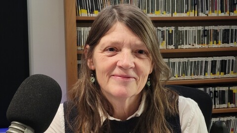 Close-up of a woman smiling at the camera in front of a wall of shelved CDs 