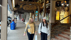 Two women chit chat as they walk down a strip of shops.