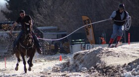 A person on skis holds one end of a rope, a person on a horse holds the other end. They are across from one another, both racing forward. 