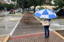 A woman waits in the rain to cross a downtown street on Oct. 2, 2026