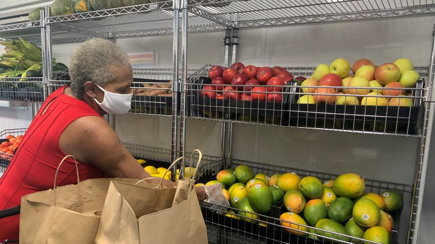 Newbill grabbing some mango, which is located on a shelf next to other fruits, including apples and lemons.