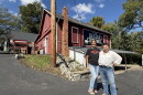 two women stand on a black driveway in front of a red barn that has a "Dexter Cider Mill" sign on it