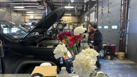 A vase of carnations in front of a car with hood open in a mechanic shop