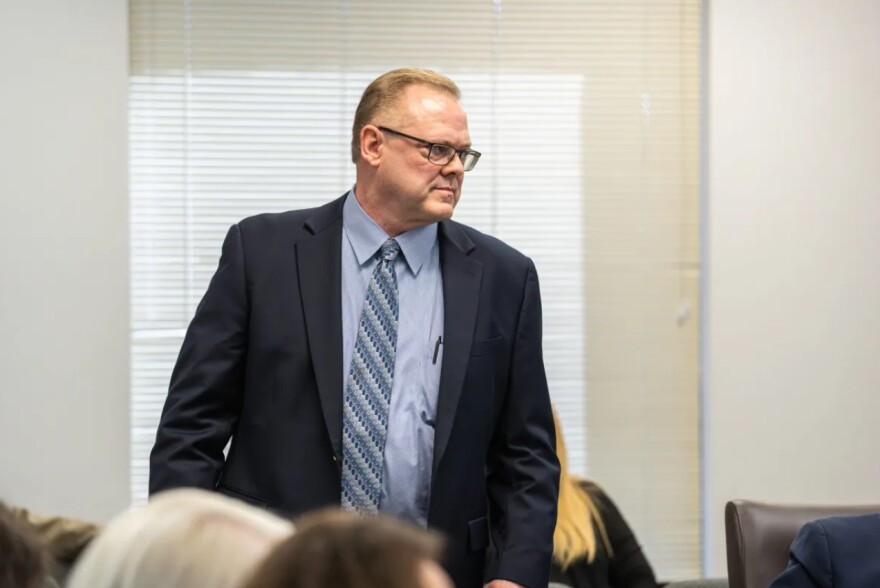 William Durham, the Tarrant Appraisal District’s director of commercial appraisals, stands in a room of people. He wears a dark blue suit, light blue shirt and blue striped tie.