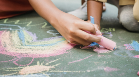 Close-up of two people drawing colorful chalk art on the pavement.