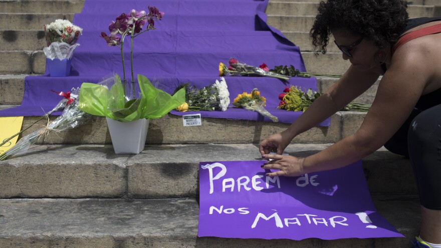 A woman positions a sign with a message that reads in Portuguese: "Stop Killing Us!" on the steps of City Hall where people gathered to pay their respects to slain council member Marielle Franco and her driver.