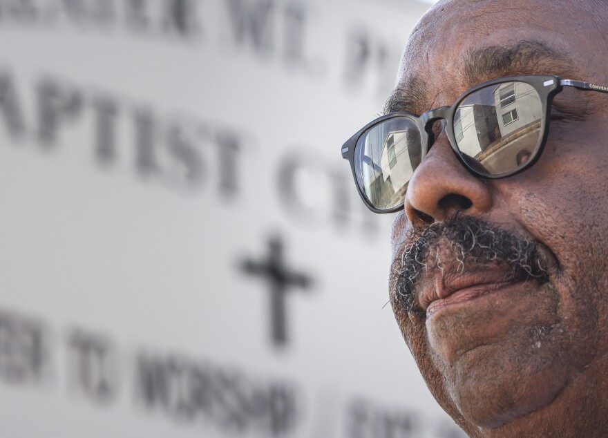 A man's face takes up the right side of the frame with a new line of homes reflecting in his sunglasses.