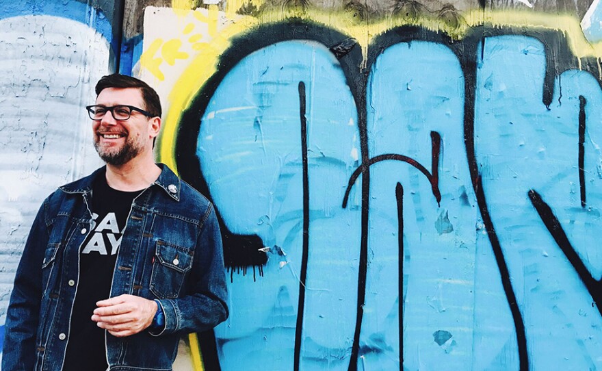 Man smiling in front of some graffiti on a wall