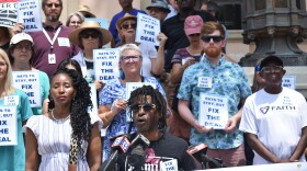 A man stands at a podium with a group gathered behind him on the steps of St. Petersburg City Hall. 