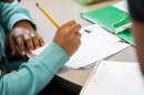 A student writes with a pencil at a table.