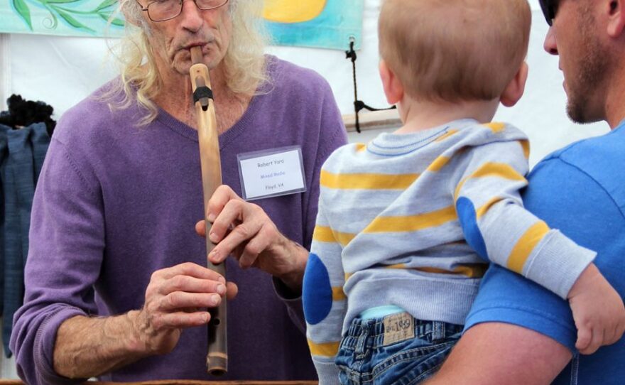 Robert Yard performs a song for a toddler using a Lakota love flute at the Cedar Key Fine Arts Festival in Cedar Key, Florida. Yard held impromptu music lessons throughout the day for patrons that were curious about playing an instrument. (Photo by Sydnei Cartwright)