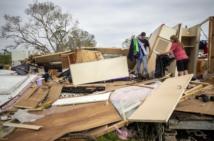 Two people pick up items after a hurricane destroyed their home.