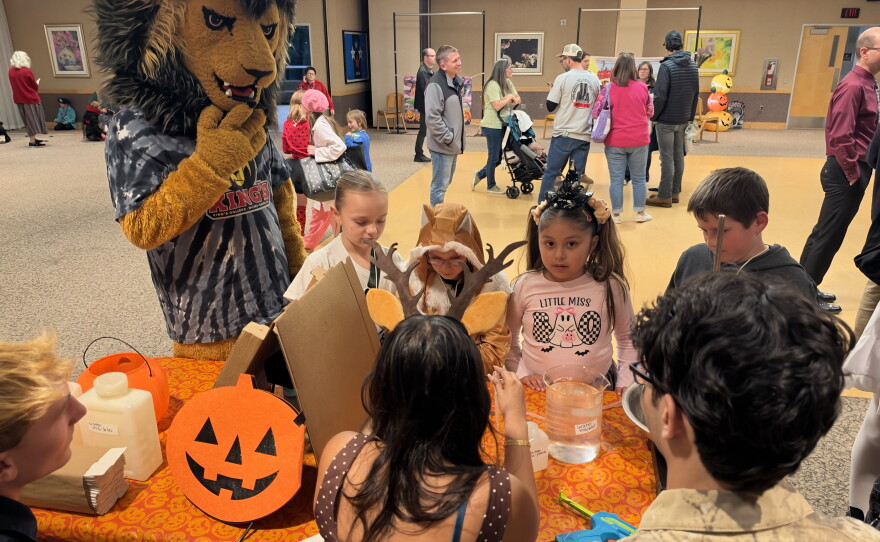 Children in Halloween costumes participate in an up-close science demonstration led by King's College students with mascot Leo the Lion.