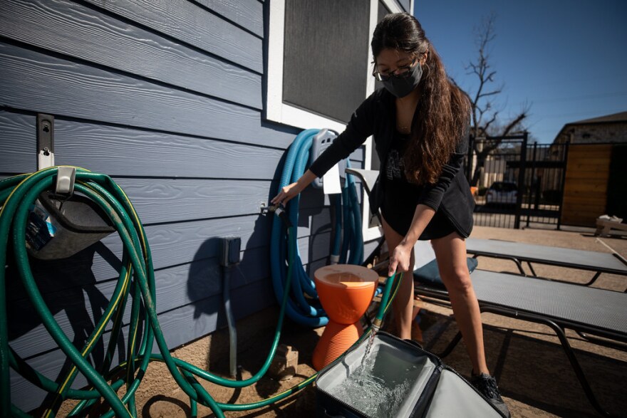 A woman fills a cooler with water from a hose. 