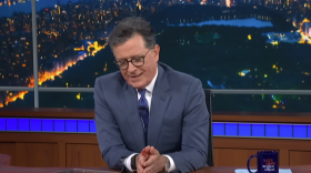 a man in a suit sits at a desk looking down