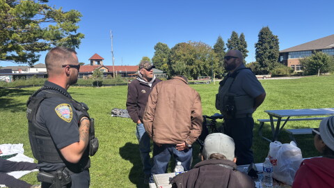 Traverse City Police Officer Matthew Kirkey and Police Support Services Worker Brad Neuder explaining the department's new enforcement efforts to a table of homeless individuals at Hull Park (Credit: IPR News / Maxwell Howard)