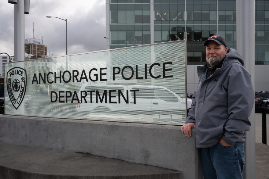 A man stands next to a sign that says "Anchorage Police Department."