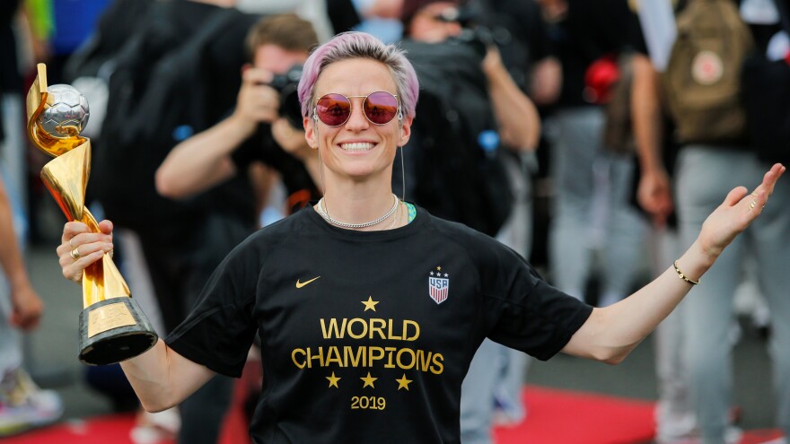 The U.S. Women's National Team is being honored by a ticker tape parade in New York Wednesday. Here, Megan Rapinoe smiles as she holds the FIFA Women's World Cup trophy as the team arrives at the Newark International Airport.