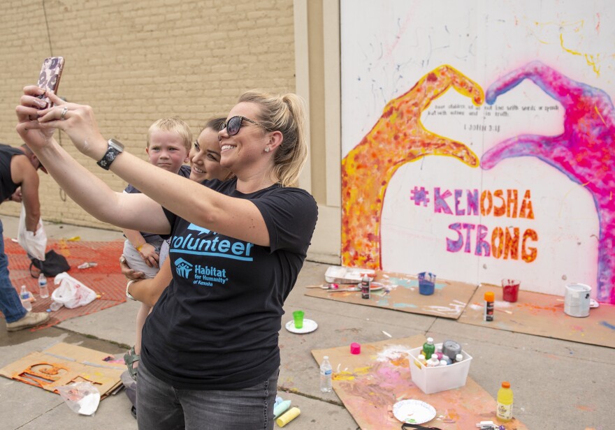 Angela Elliott (C) takes a picture in front of a mural she helped to create on the boarded windows of a business in the Uptown neighborhood of Kenosha, WI on August 28.