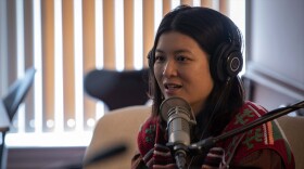 Jiemei Lin wears a pair of headphones and a crocheted sweater on a tan loveseat.