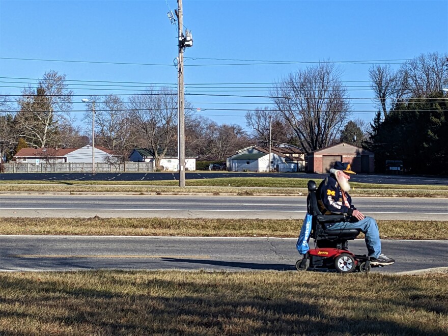 Man in a motorized wheelchair travels on a street with no sidewalk