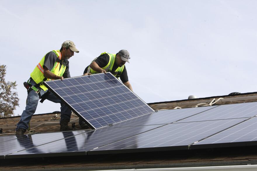 Workers install a rooftop solar panel on a home.