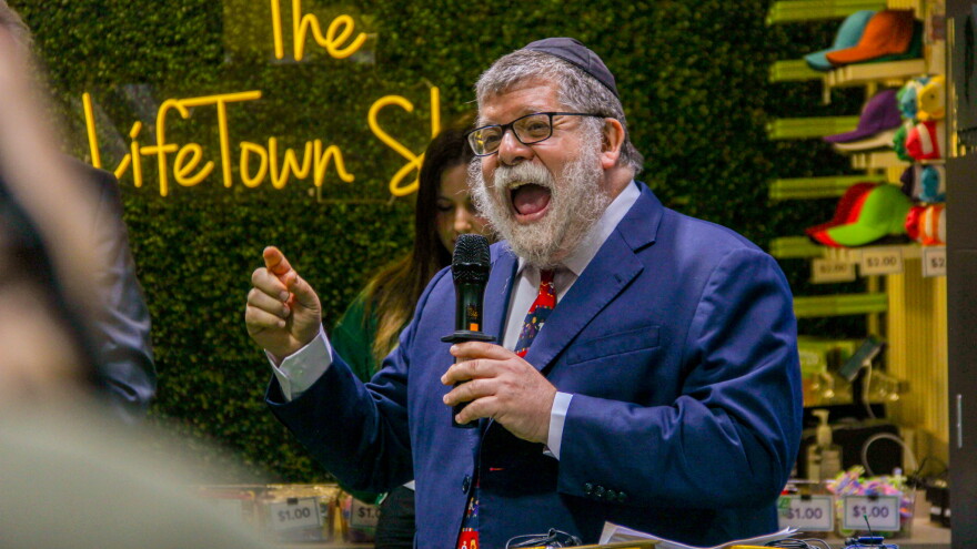 A rabbi in a bright suit speaks enthusiastically into a microphone. 