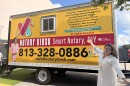 A woman in a white dress poses in front of a trailer that has Notary Kiosk Smart Notary DIY in white letters across the front
