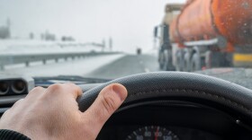 driver hand on the steering wheel inside the car while overtaking on the left lane of a tanker truck with a tank of dangerous flammable, combustible cargo, gasoline, diesel fuel