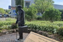 A statue of a young man with a suitcase and cane is visible in a park in downtown Petoskey. In the foreground, a gold plaque reads "Ernest Miller Hemingway." 