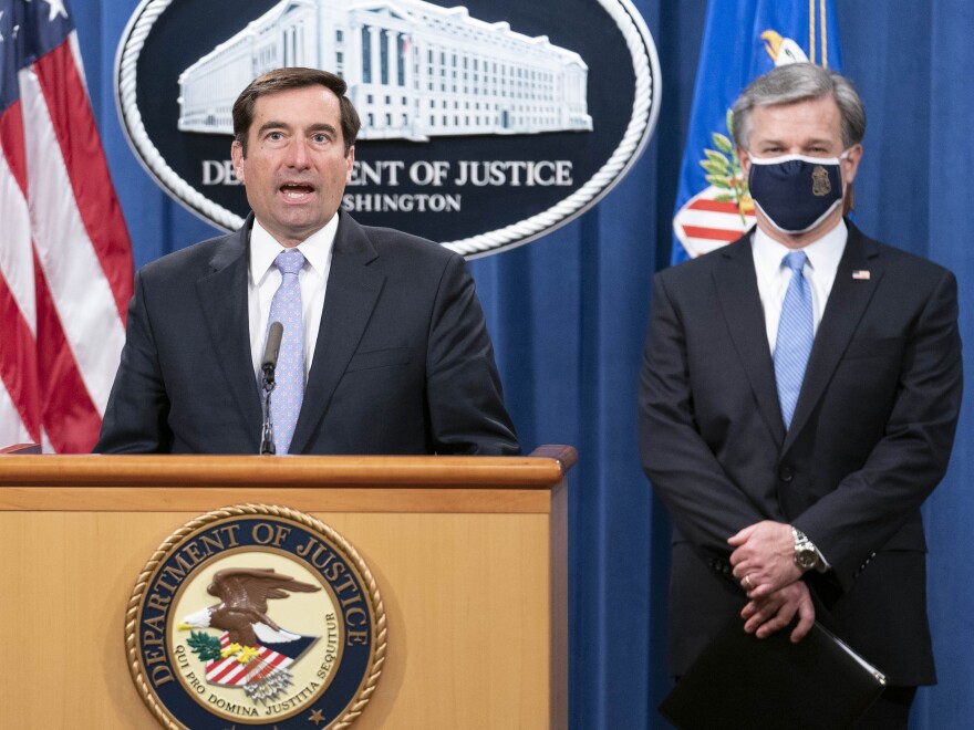 Assistant Attorney General for National Security John Demers speaks during a virtual news conference at the Department of Justice, Wednesday, Oct. 28, 2020 in Washington, as FBI Director Christopher Wray looks on. The Justice Department has charged eight people with working on behalf of the Chinese government to locate Chinese dissidents and political opponents living in the U.S. and coerce them into returning to China. Five of the eight were arrested Wednesday morning. (Sarah Silbiger/Pool via AP)