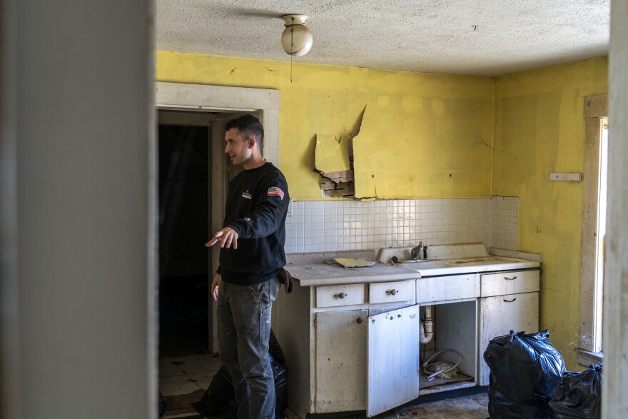 A man stands in an old apartment with cracked and broken finishing