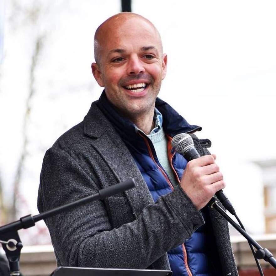 State Senator Adam Hinds holds a microphone at an outdoor event.