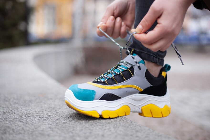Girl tying shoelaces on multi-colored sneakers of yellow, white, black and blue on the street