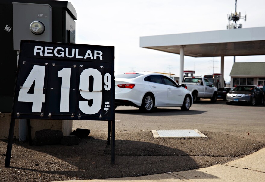 Photo of a gas station with cars lined up at the pumps. In the foreground, a sign shows that regular gas is $4.19 per gallon. 