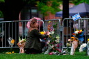 A woman places a bouquet of flowers along a guardrail where other flowers have been left.
