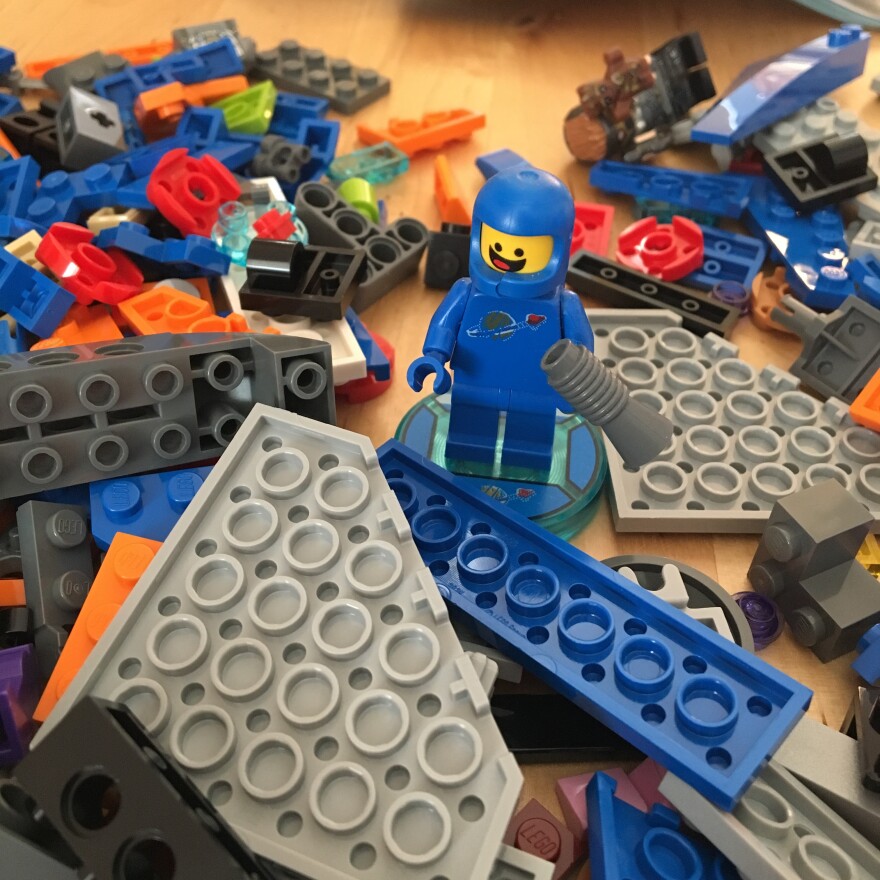 A LEGO minifigure stands among pieces ready to be assembled