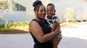 A woman smiles at the camera while holding her young son 
