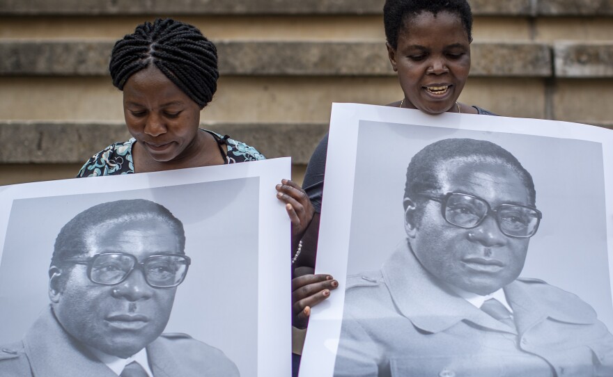 Women in the stands at the National Sports Stadium hold posters of former president Robert Mugabe.