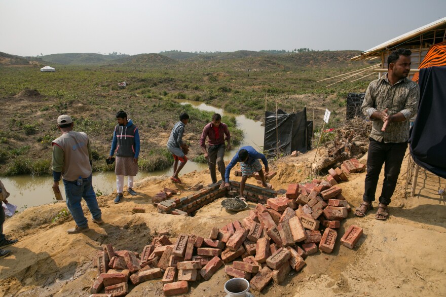 Men build a brick and cement toilet in the Kutupalong refugee camp. The new toilet will replace the open-pit toilets — covered with plastic for privacy — that can be seen in the background.