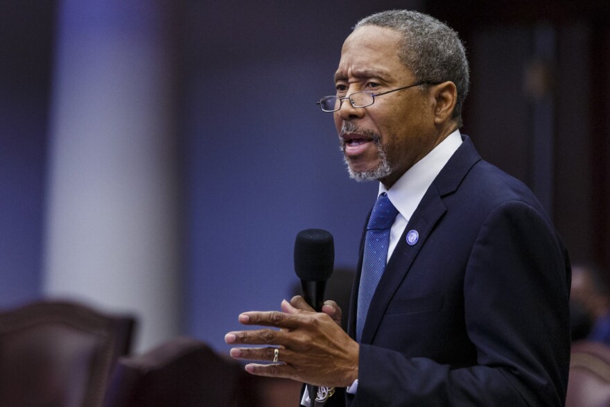 Elderly african american man in glasses and suit and tie speaks into microphone 