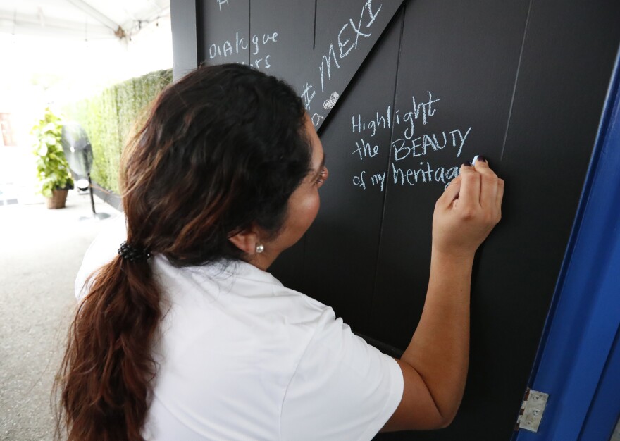 Ivette Diaz writes in chalk on one of the doors from the <em>Common Ground</em> installation. She is with the Libre Institute, one of the groups behind the project, which focuses on discussions around immigration.