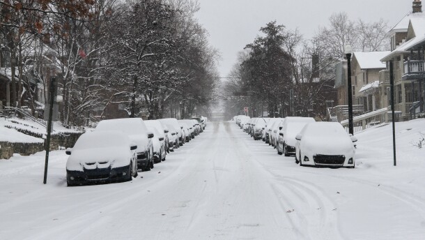 Snow-covered cars line either side of an unplowed side street. 