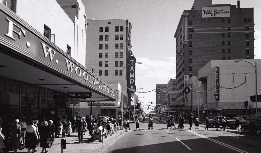 A vintage black/white photo showing F.W. Woolworth to the left with a street in the middle and tall buildings in the background