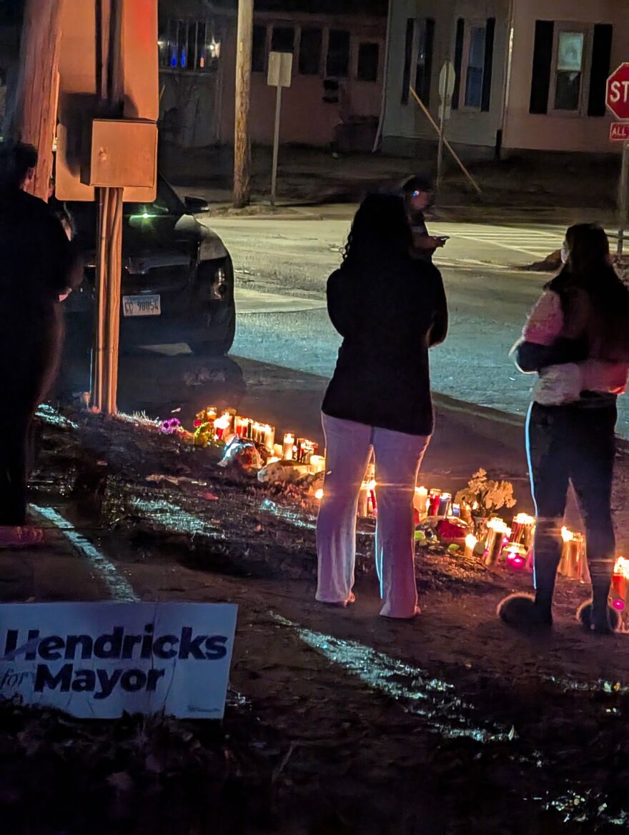 people stand on a darkened street illuminated by a candlelight vigil.