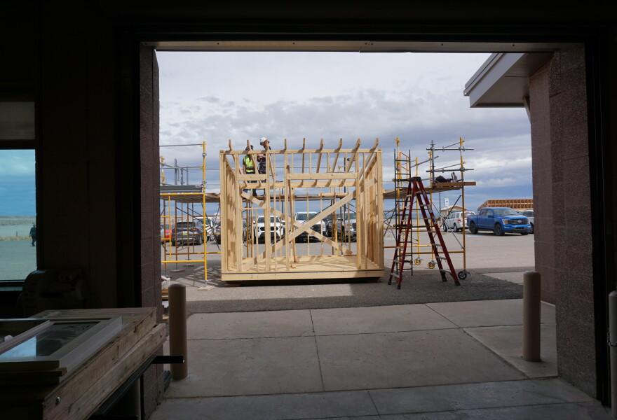 Two students work on the top of a framed, wooden structure outside.