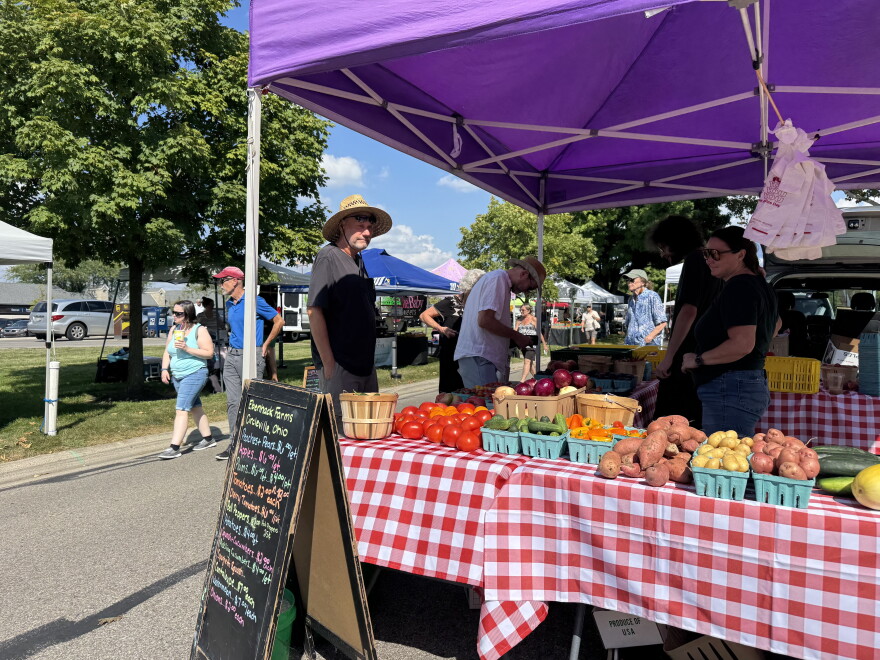 People standing by a booth with a variety of produce products and two vendors.